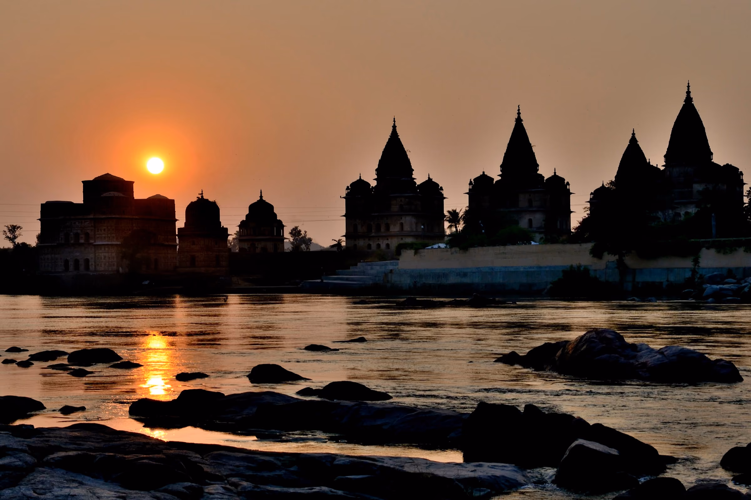 Orchha’s royal cenotaphs against the setting sun, above the rocks of the Betwa River